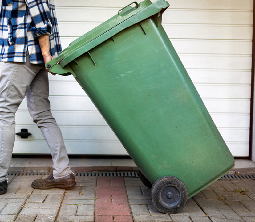 Person moving a green wheeled trash bin